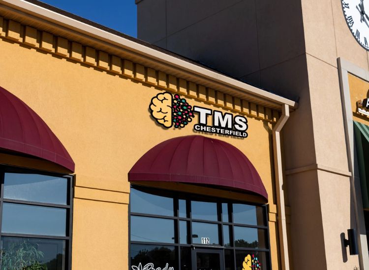Exterior of a commercial building featuring the Storefront TMS Logo for Palmier TMS, with a yellow facade, maroon awnings, and entrance number 112, indicating a mental health clinic specializing in Transcranial Magnetic Stimulation.