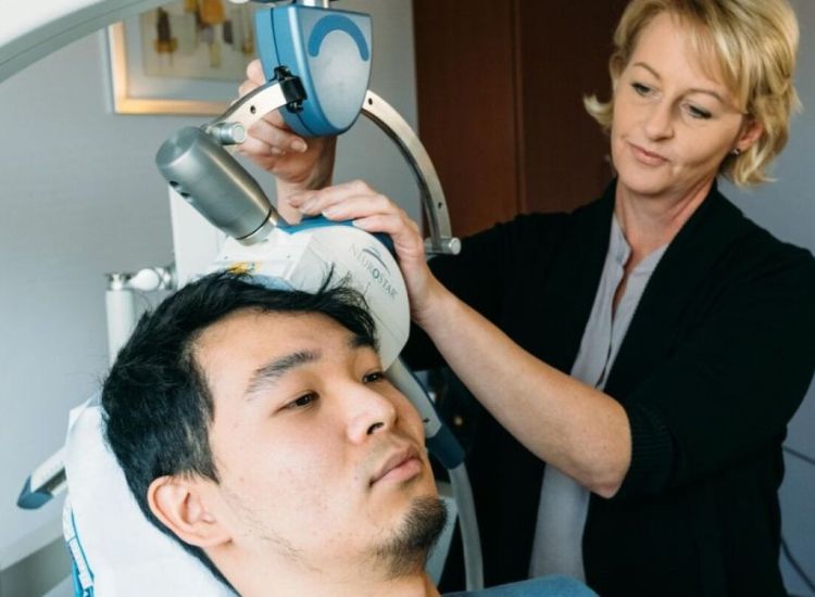 Healthcare professional positioning a NeuroStar TMS device on a seated patient’s head in a clinical setting.